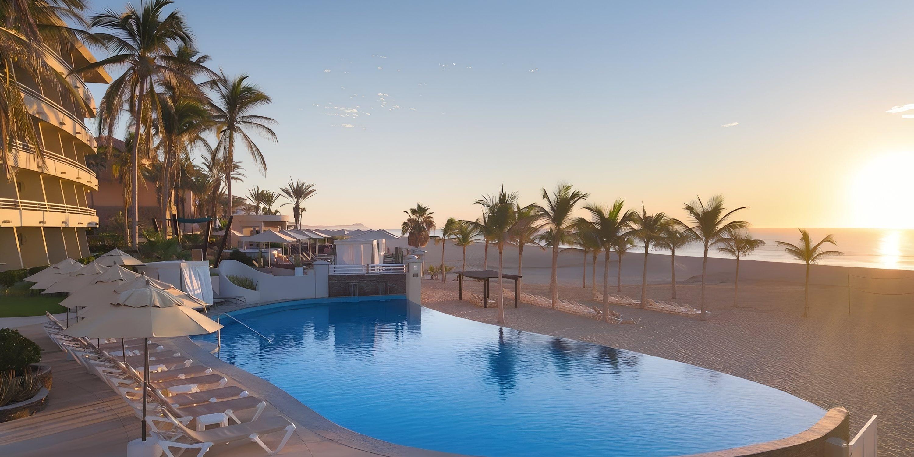 Barcel&oacute; Grand Faro Los Cabos pool at sunrise, ideal for a destination wedding, with chairs and palm trees.
