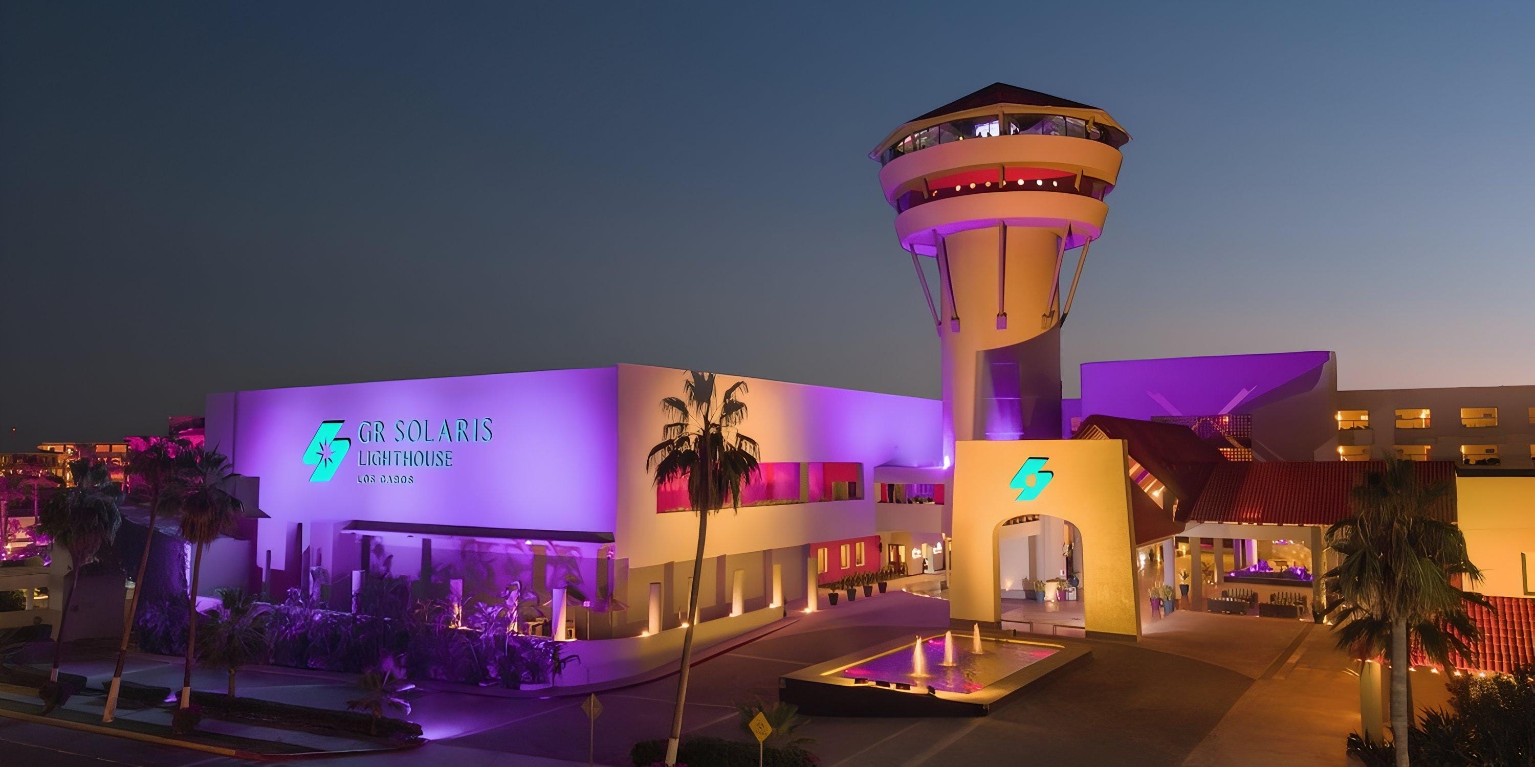 Barcel&oacute; Grand Faro Los Cabos aglow in purple at dusk, perfect for a destination wedding backdrop.