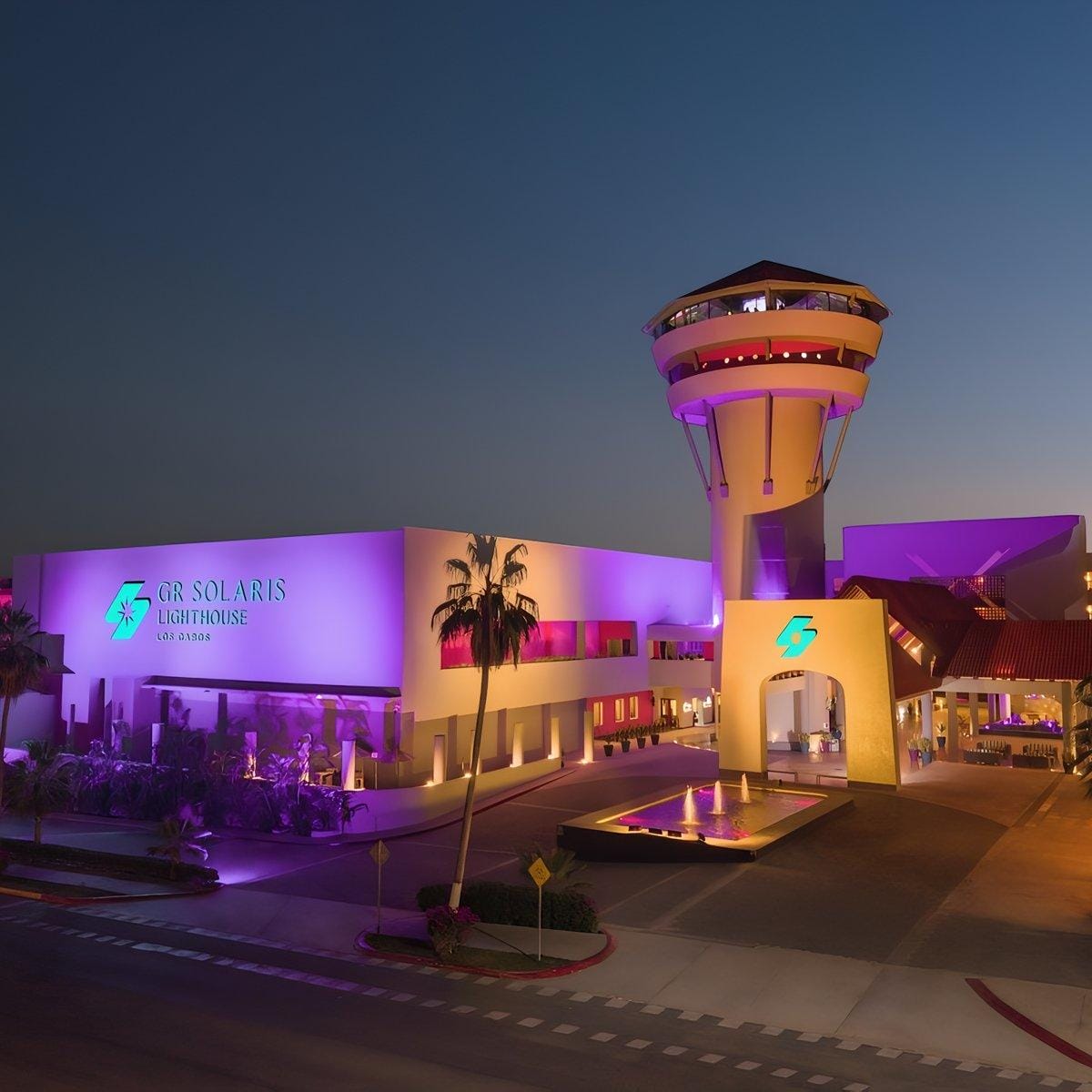Barcel&oacute; Grand Faro Los Cabos hotel at dusk, purple lights and tower aglow&mdash;perfect for a destination wedding.