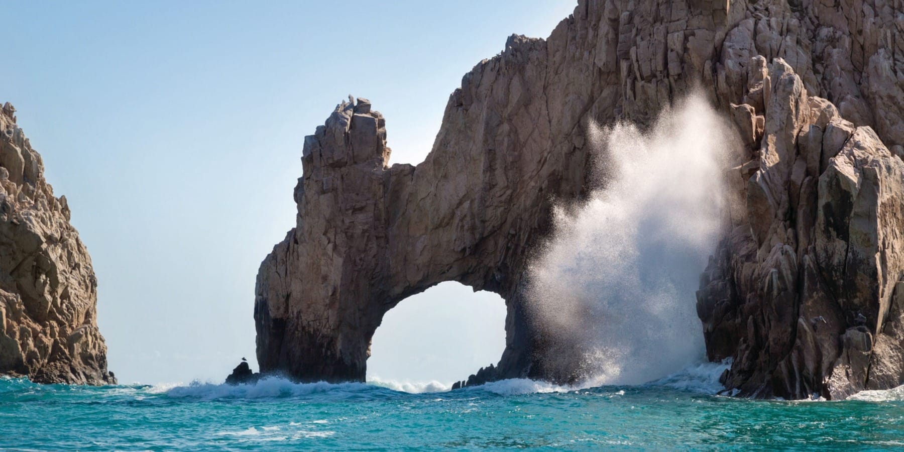 Scenic ocean rock arch with waves crashing, perfect backdrop for a destination wedding under clear skies.