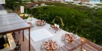 Outdoor wedding dining setup with decorated tables and a dance floor by lush greenery and the beach.