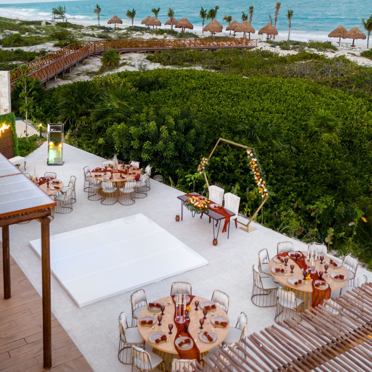 Destination wedding reception outdoors featuring round tables, a dance floor, and an ocean backdrop.