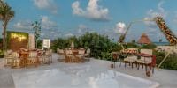 Destination wedding setup outdoors with tables, chairs, floral arrangements, and a dance floor beneath clouds.