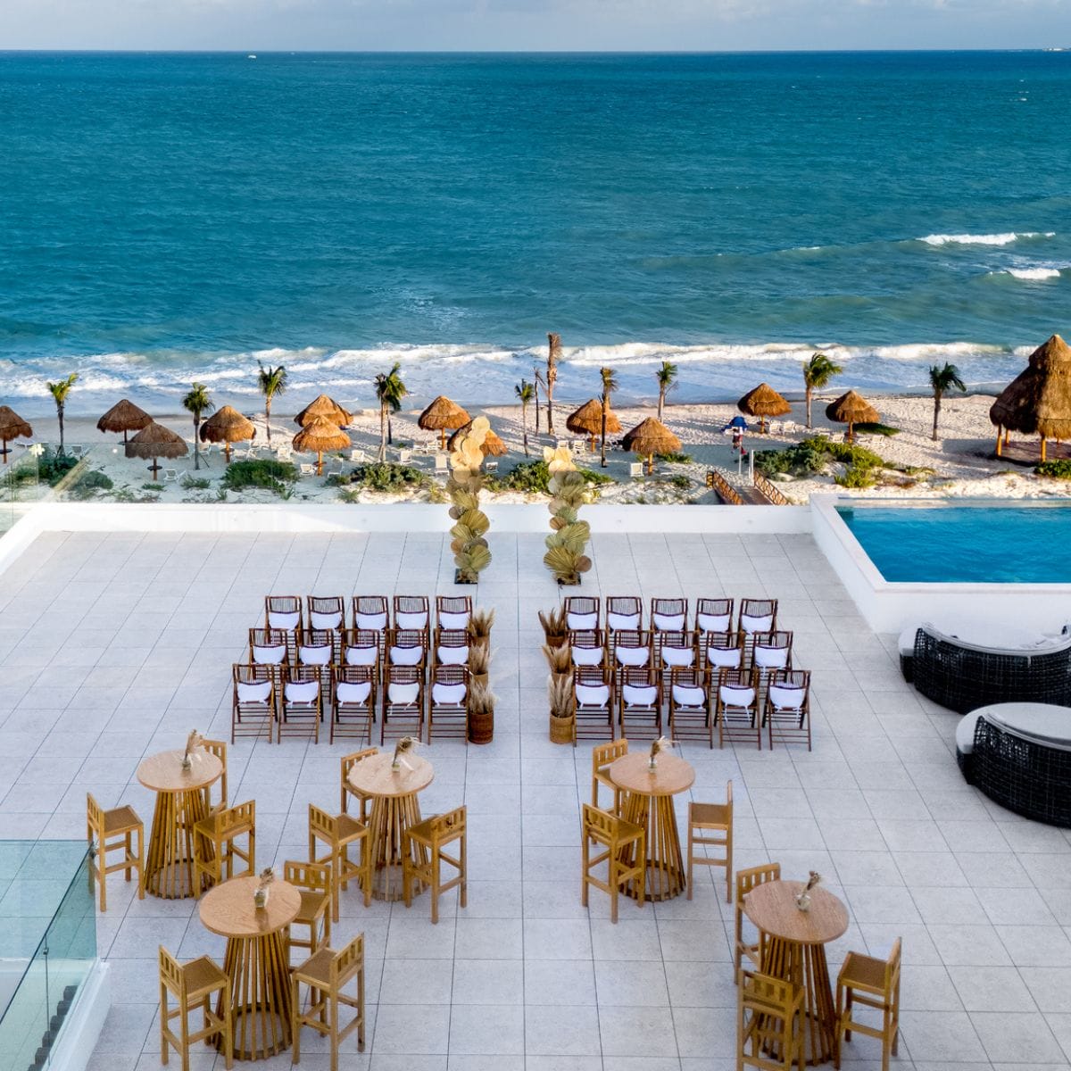Destination wedding setup on the beach with rows of chairs, tables, and an ocean view in the background.