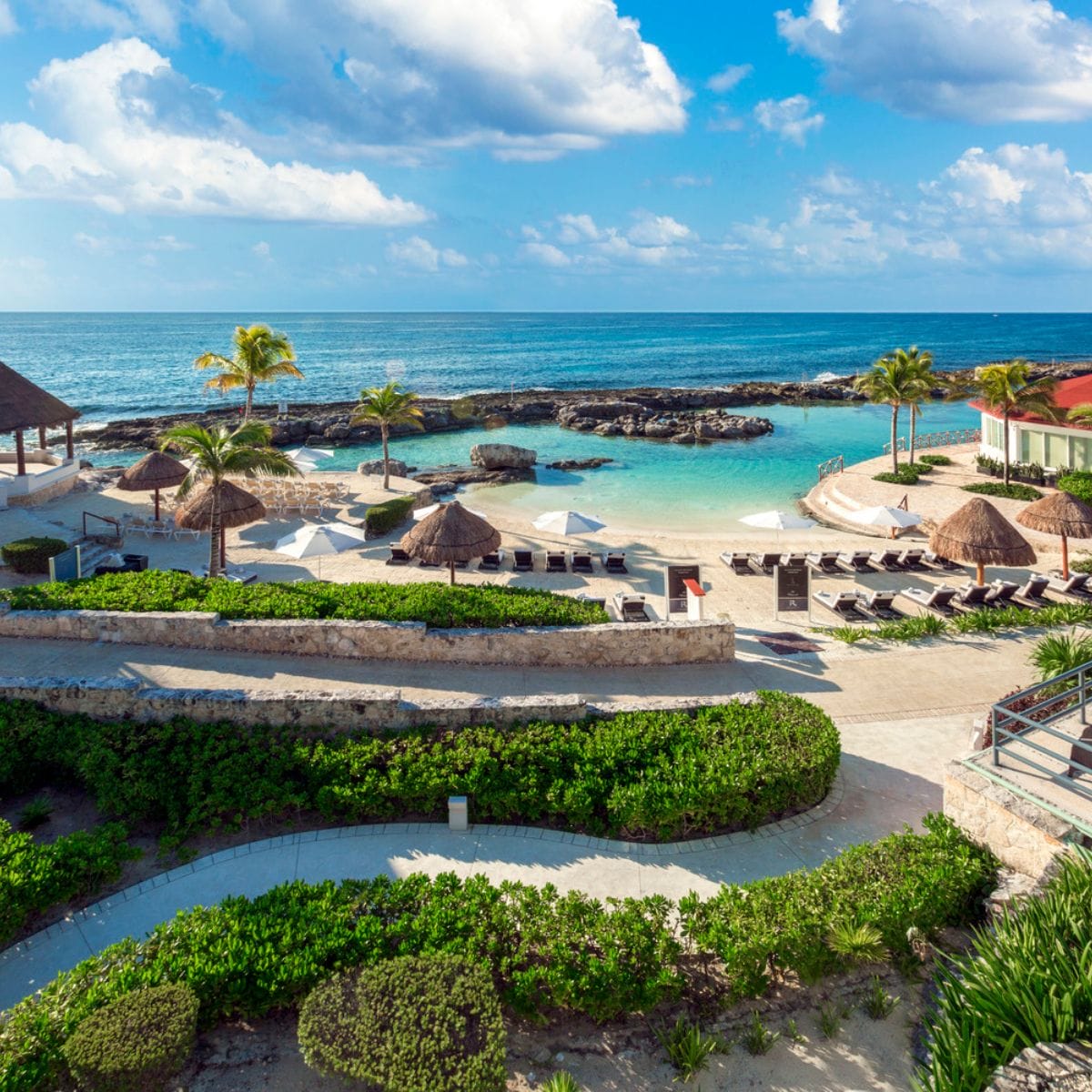 A beachfront resort, perfect for a destination wedding, with lounge chairs, thatched umbrellas, and blue water.