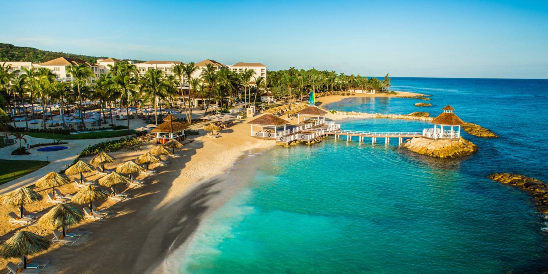 Aerial view of a tropical beach resort, ideal for a destination wedding, with palm trees and cabanas.