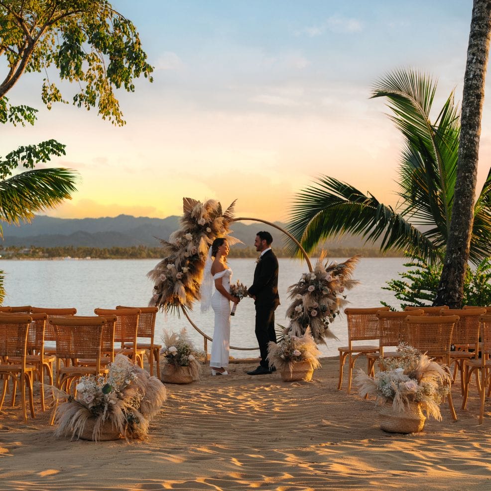 At sunset, a bride and groom hold hands at a destination wedding altar on the beach.
