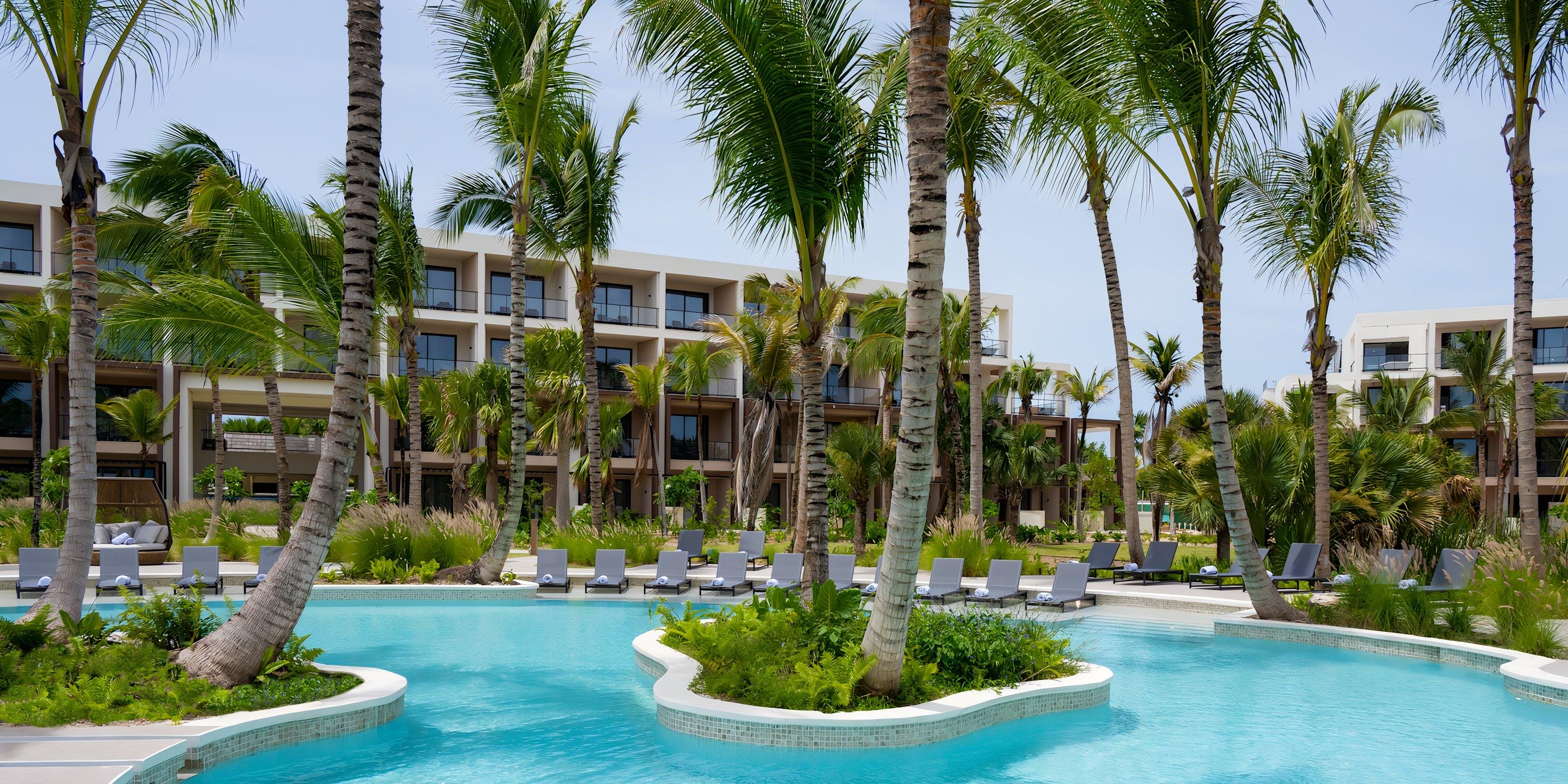Hilton Cancun Mar Caribe pool, perfect for a destination wedding, with lounge chairs, palms, and modern buildings.