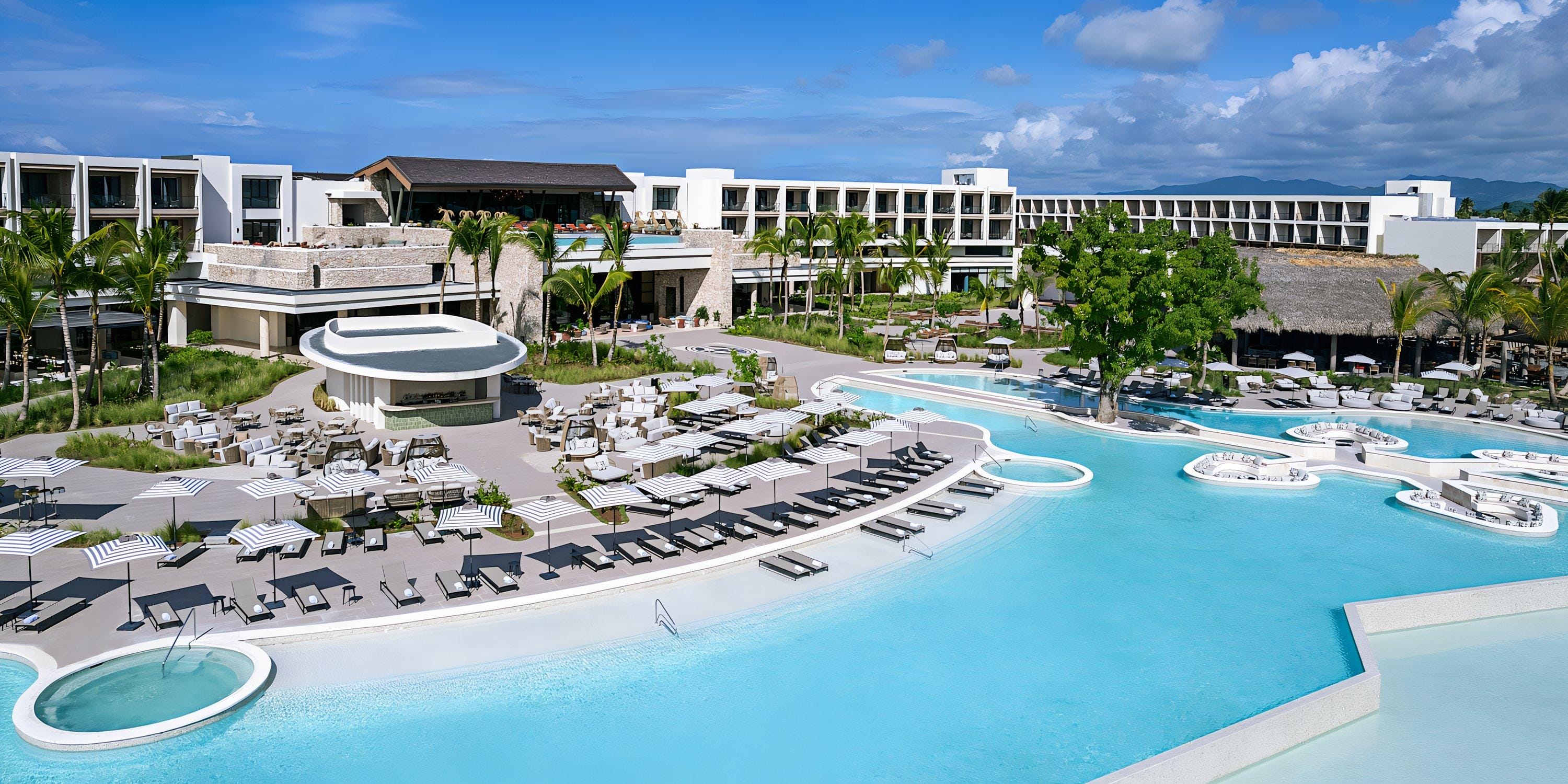 Hilton Cancun Mar Caribe: pool area with lounge chairs, umbrellas, modern buildings—ideal for a destination wedding.