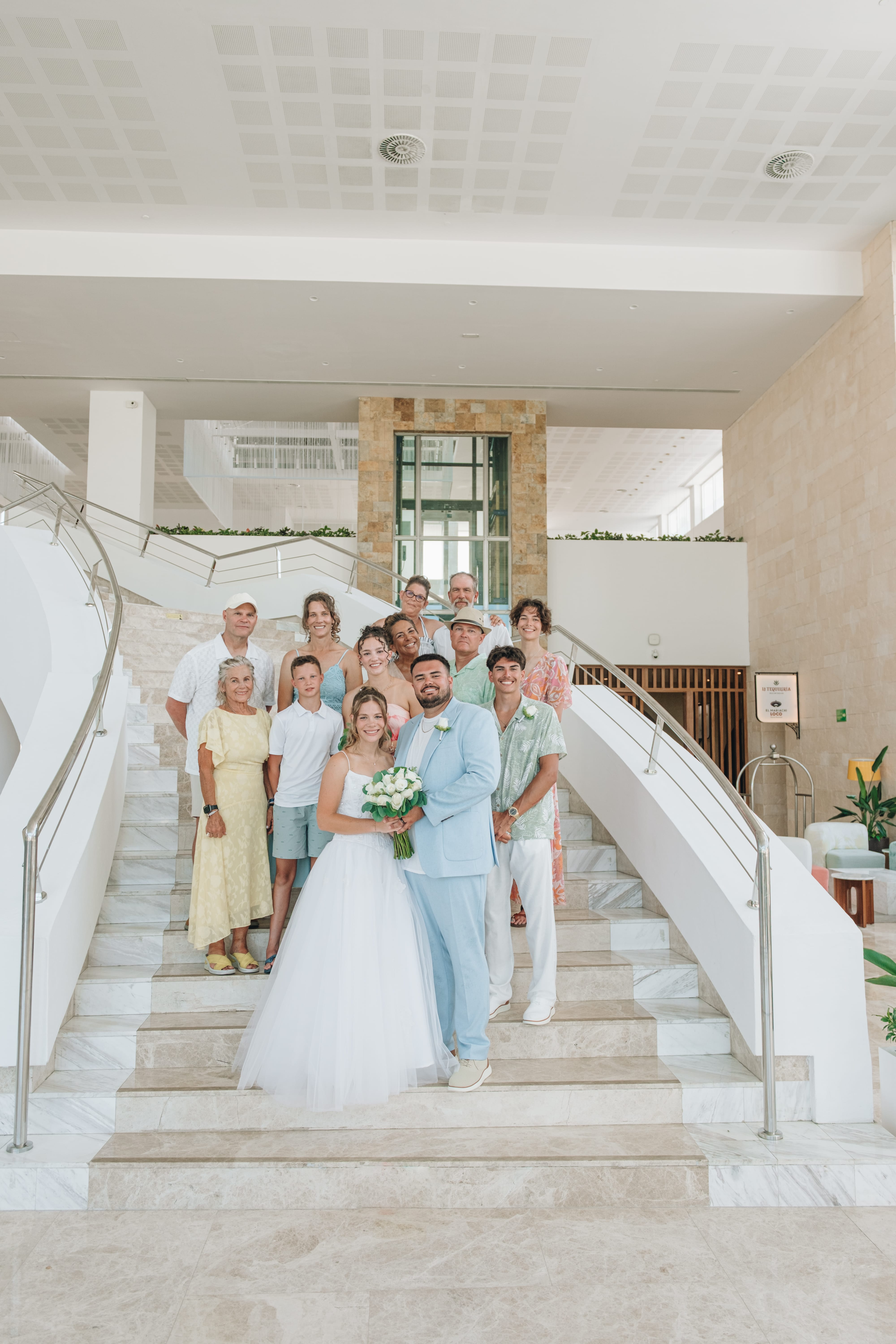 Kayleigh and Isaac pose with family on marble stairs at their destination wedding venue.