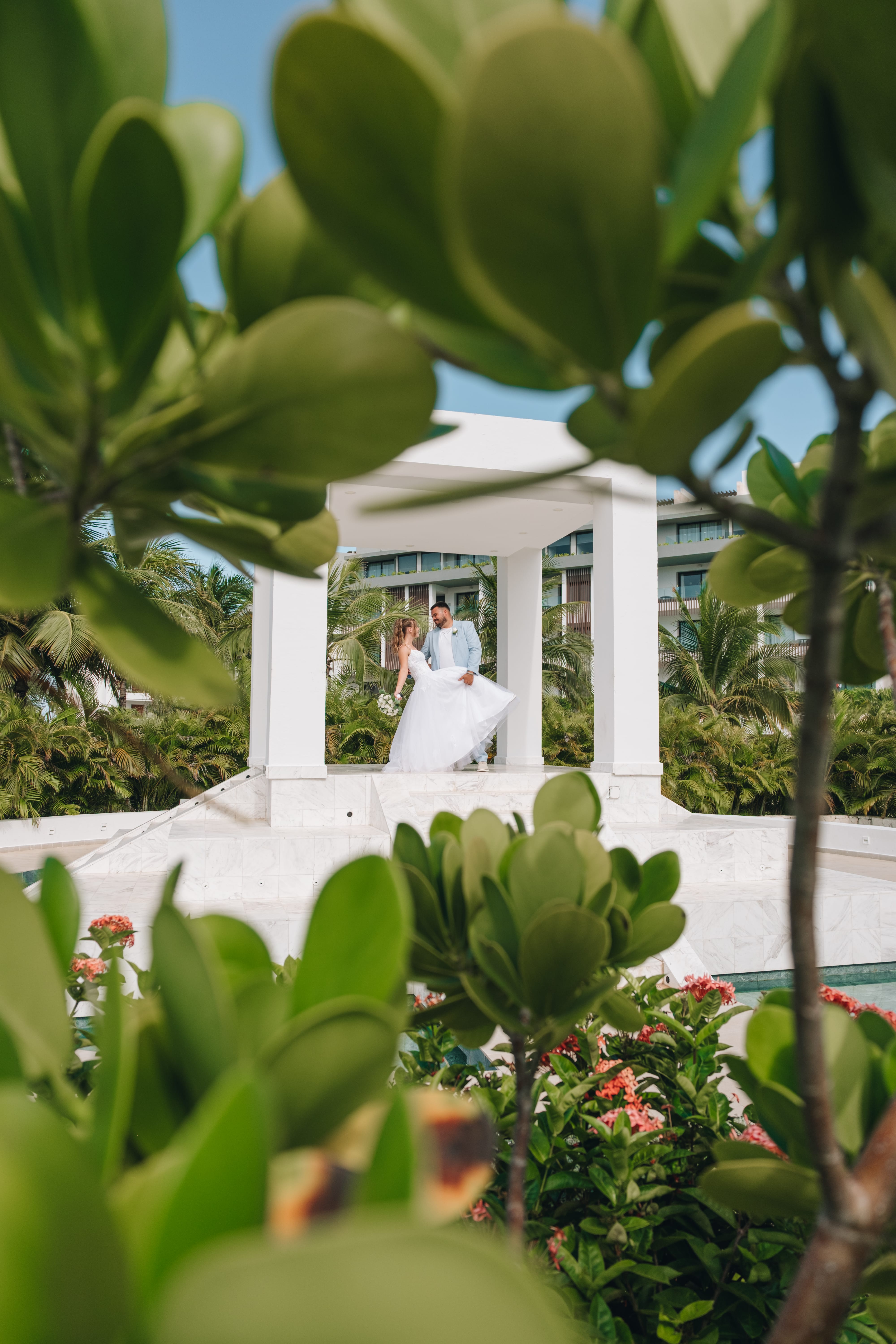 Kayleigh and Isaac stand under a white gazebo at their destination wedding, surrounded by flowers.