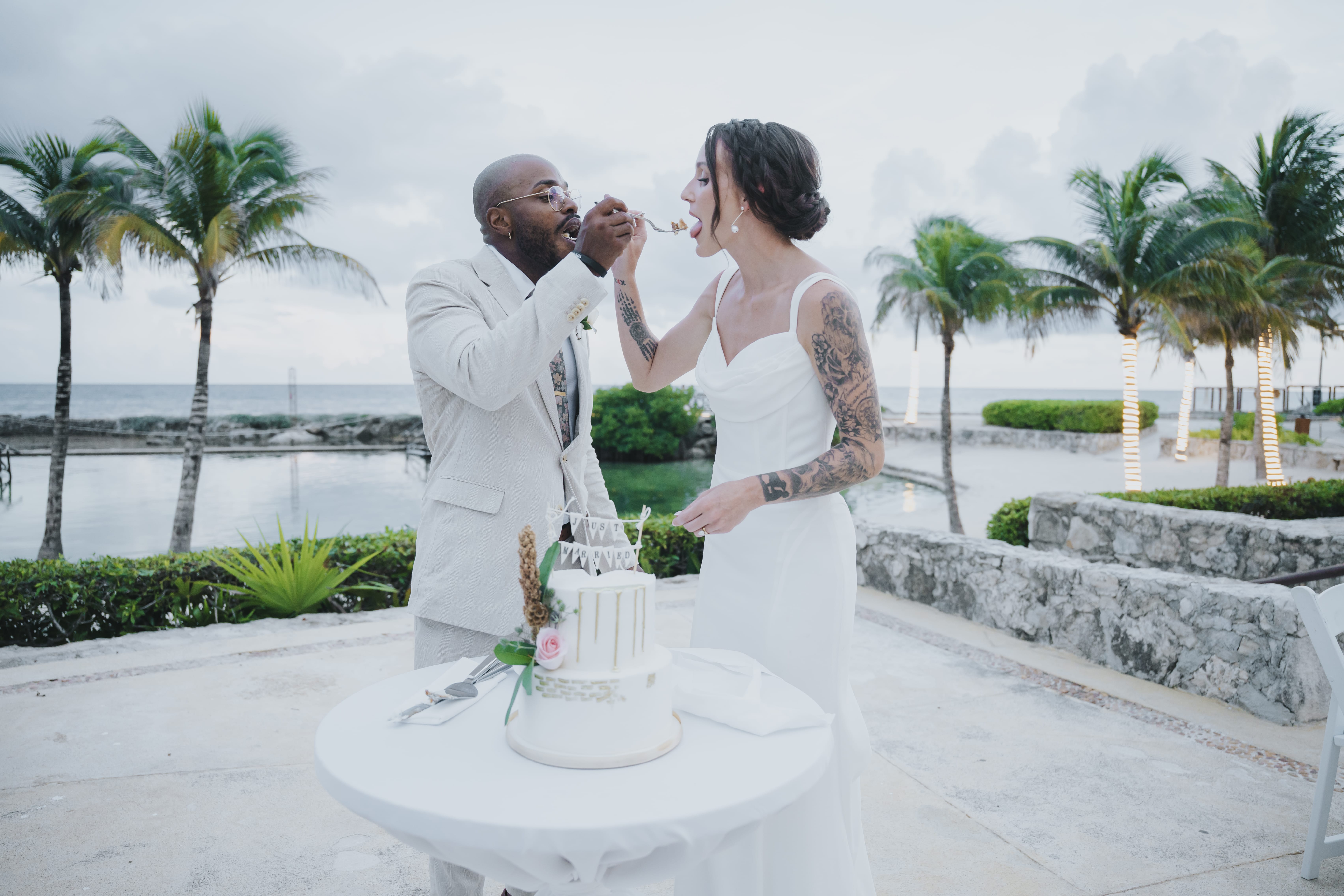 At their destination wedding by the water, Madison and Blake share cake and laughter outdoors.