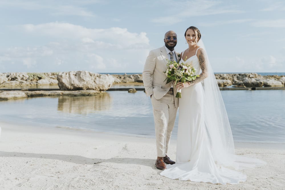 Madison and Blake at their destination wedding on a beach, rocks and water as backdrop.