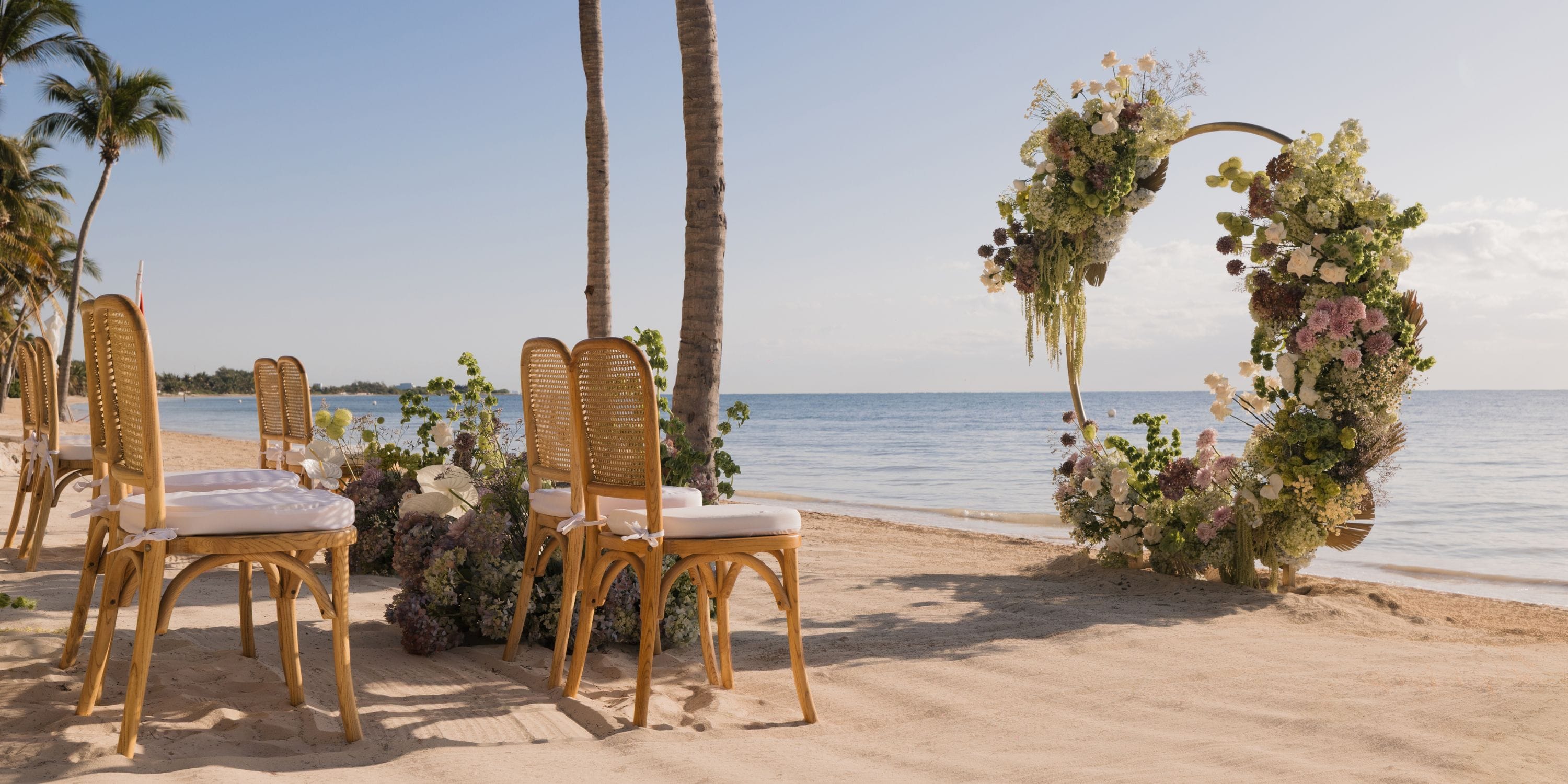 Destination wedding setup at Royalton Riviera Cancun with chairs, floral arch, and ocean backdrop.