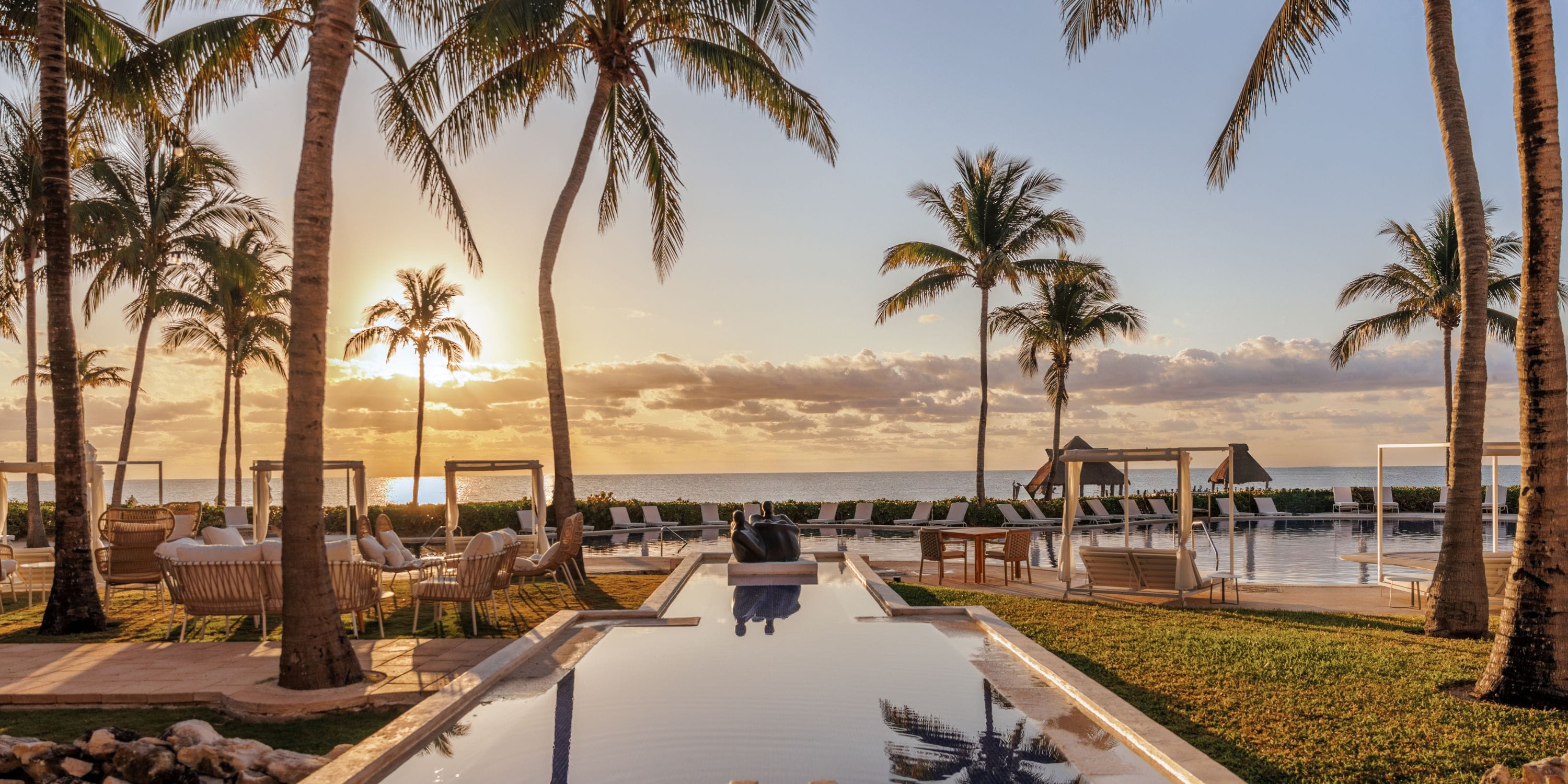 Palm trees and lounge chairs ring a pool at sunrise, perfect for a destination wedding by the ocean.
