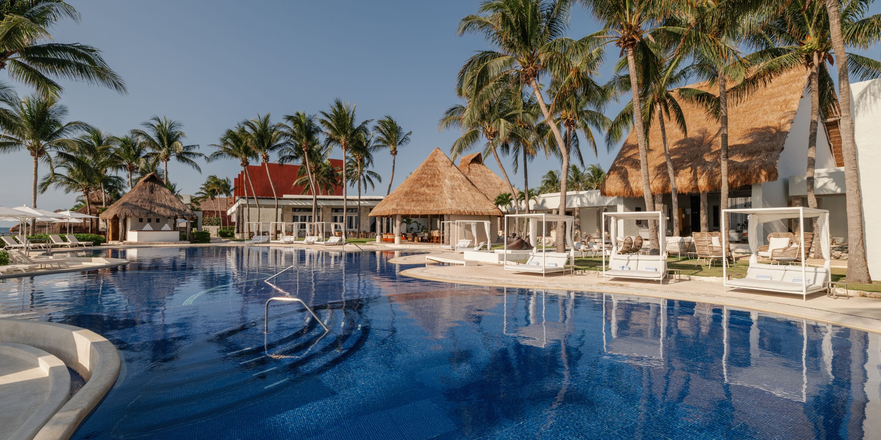 Royalton Riviera Cancun's pool&mdash;a dream destination wedding spot with palm trees and thatched roofs.