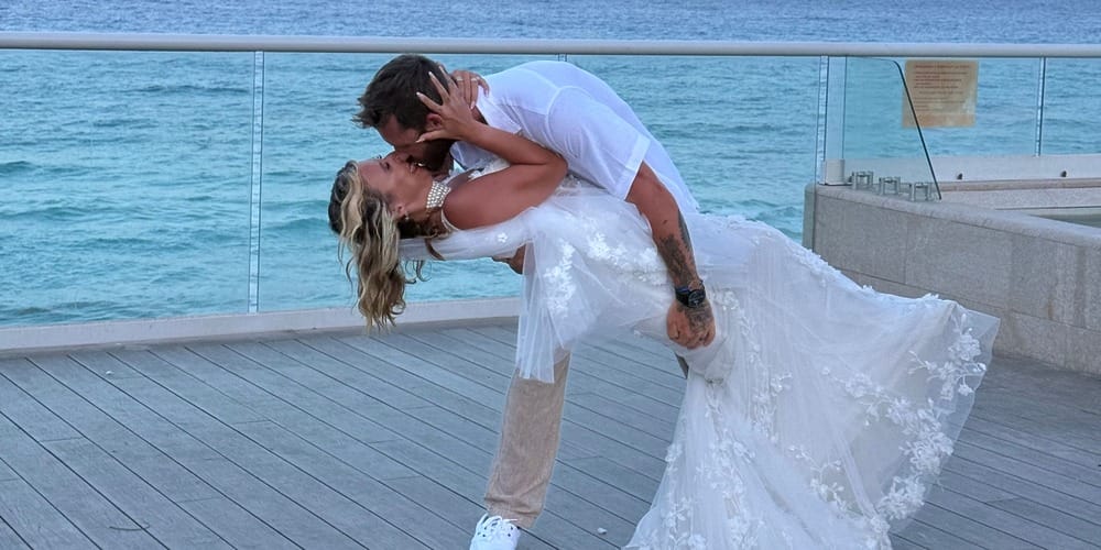 Bride and groom share a kiss on the boardwalk by the ocean at their destination wedding.