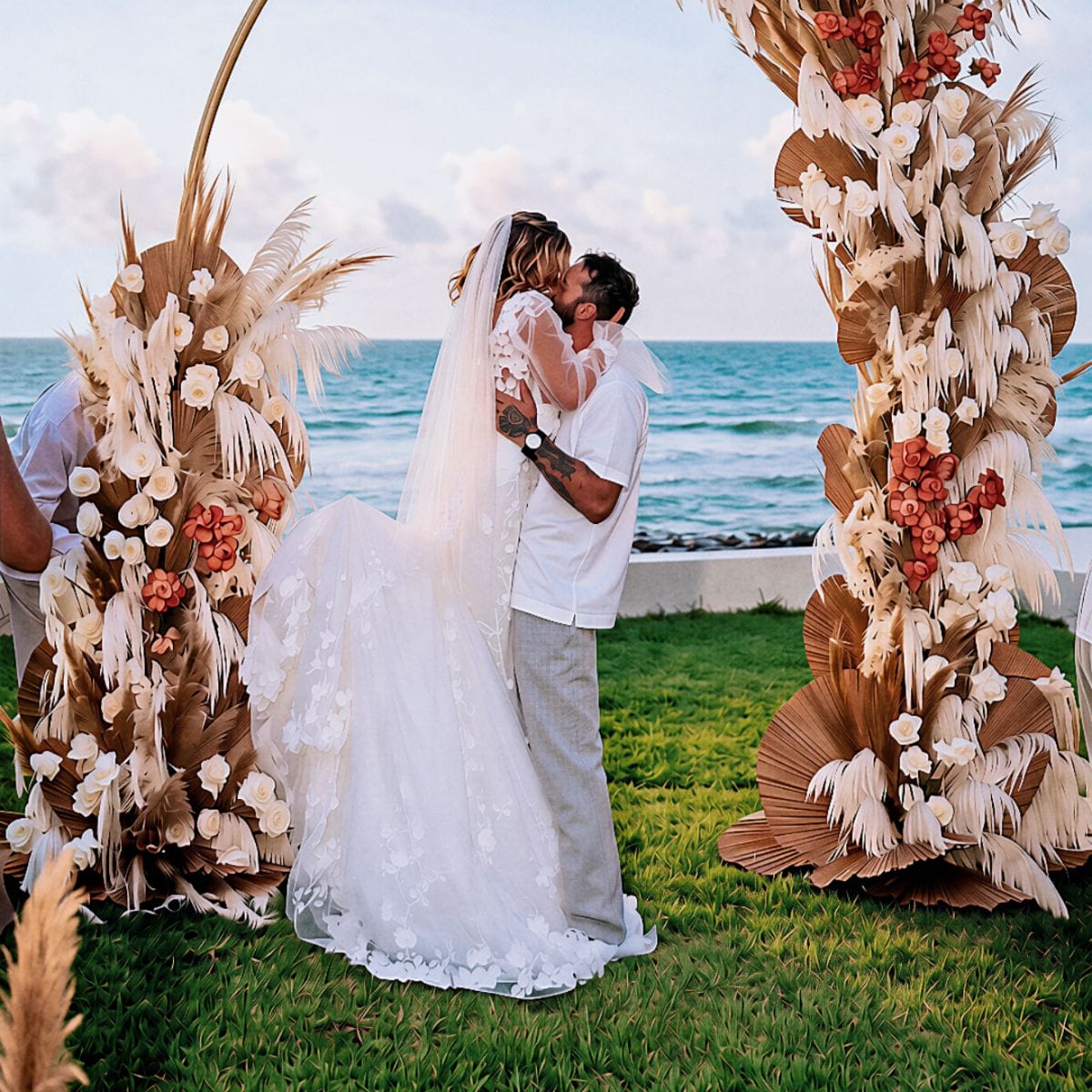 Kayleigh and Isaac kiss under a floral arch at their oceanfront destination wedding ceremony.