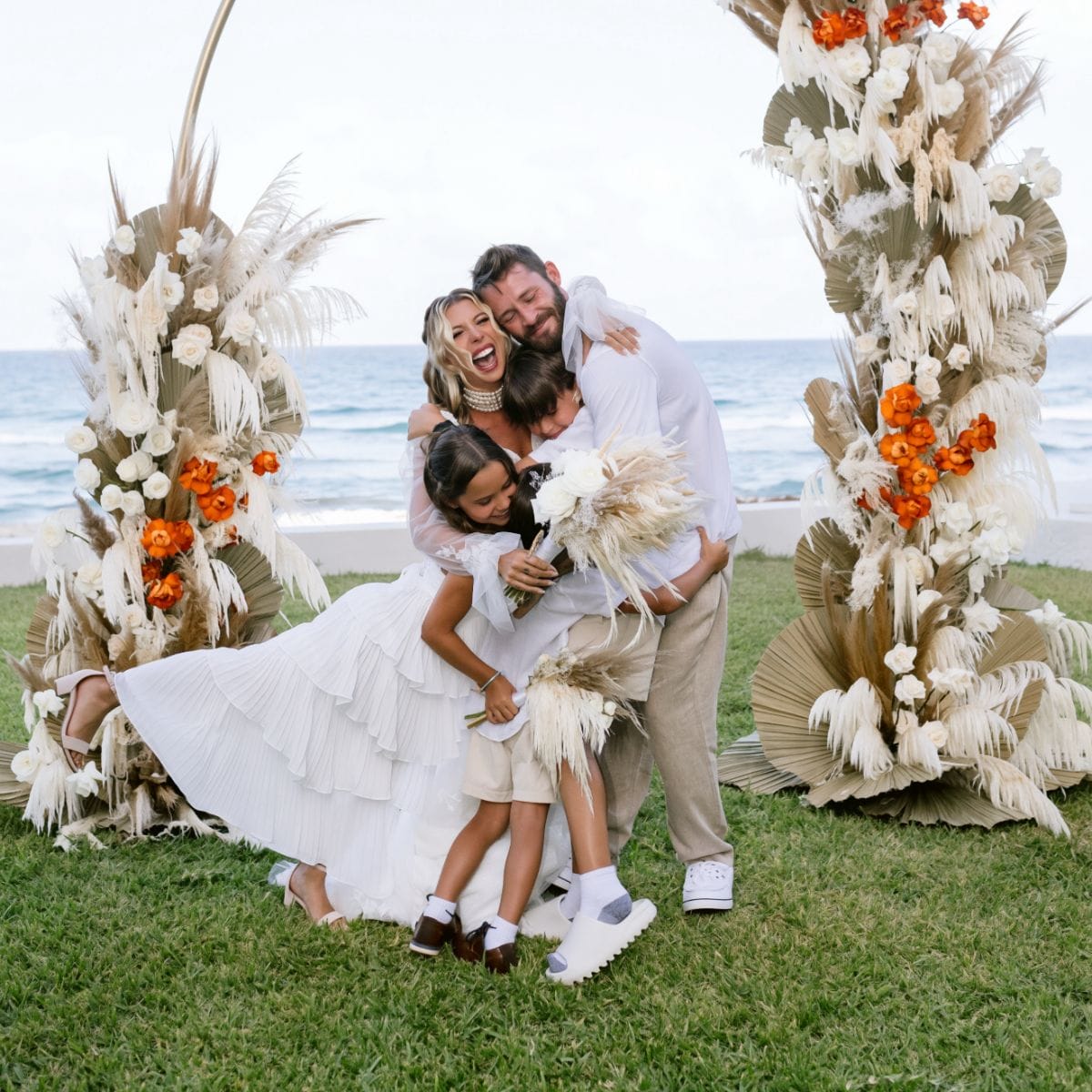 A family smiles by the ocean during Kayleigh and Isaac's beachfront destination wedding.