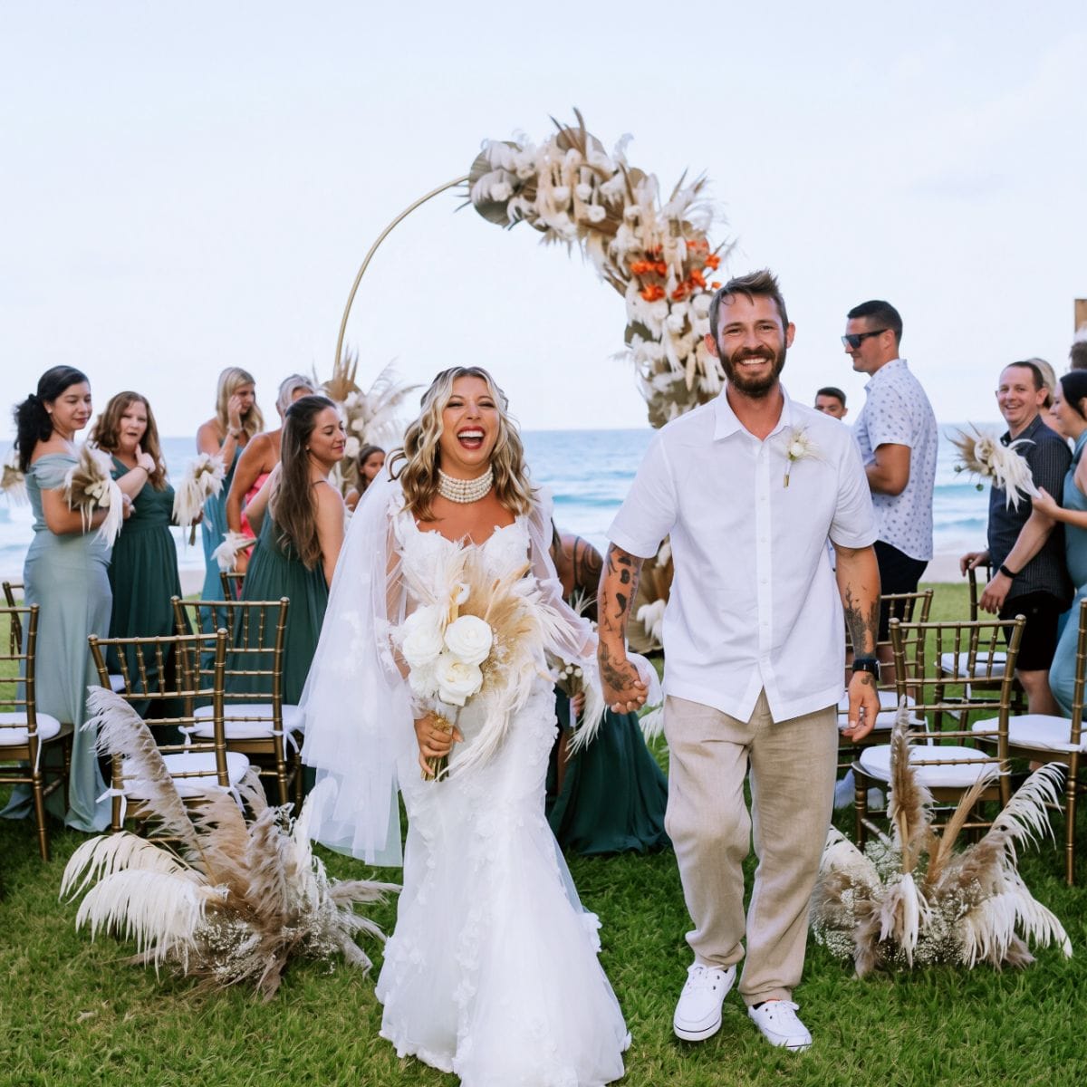 Kayleigh and Isaac walk down the aisle at their destination wedding as guests applaud.
