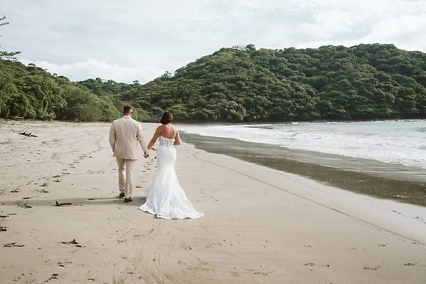 Bride and groom holding hands on a sandy beach during their destination wedding in Costa Elena.