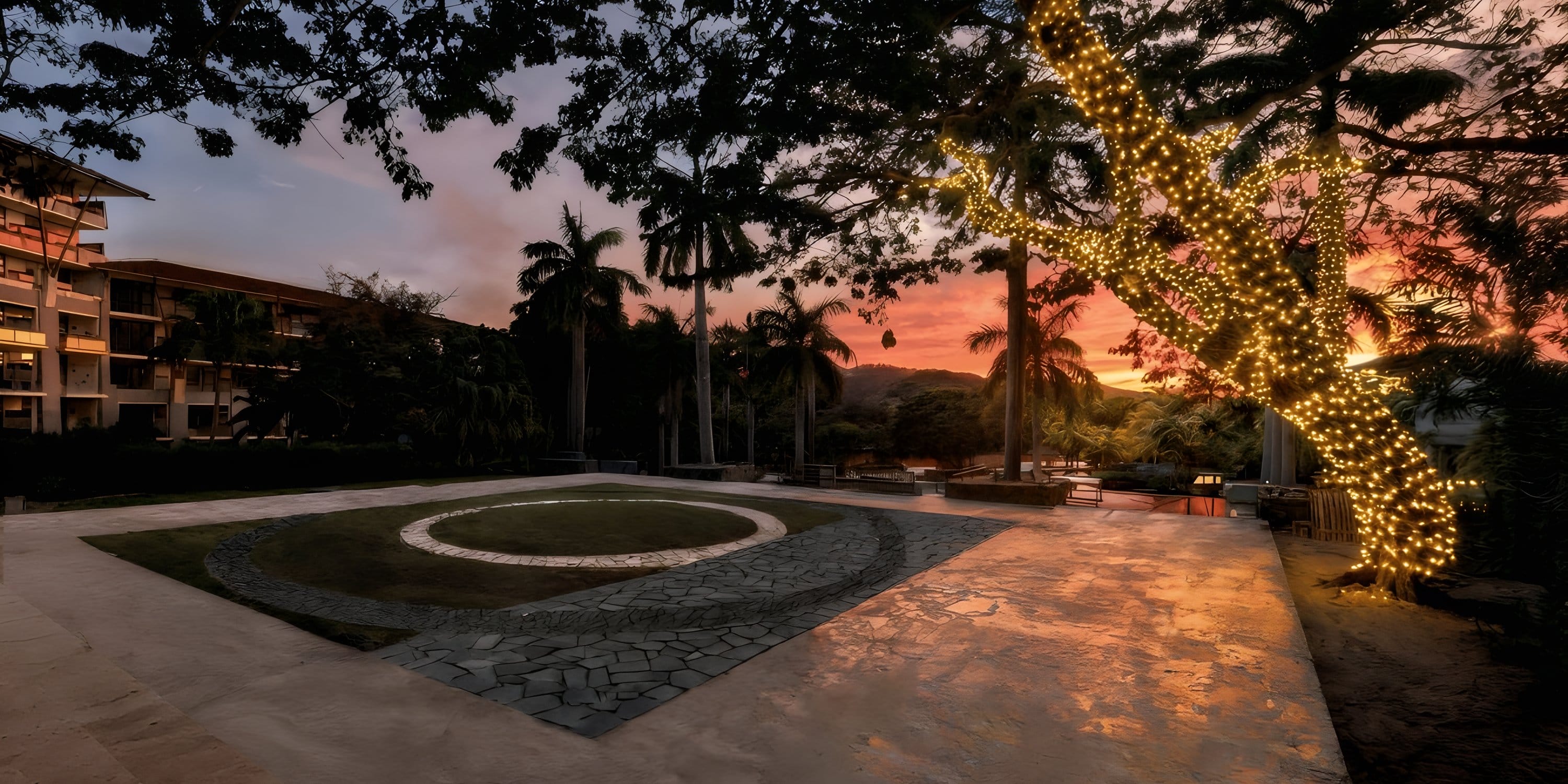 Sunset at Dreams Las Mareas: palms, lit tree, circular grass plaza—ideal for a destination wedding.