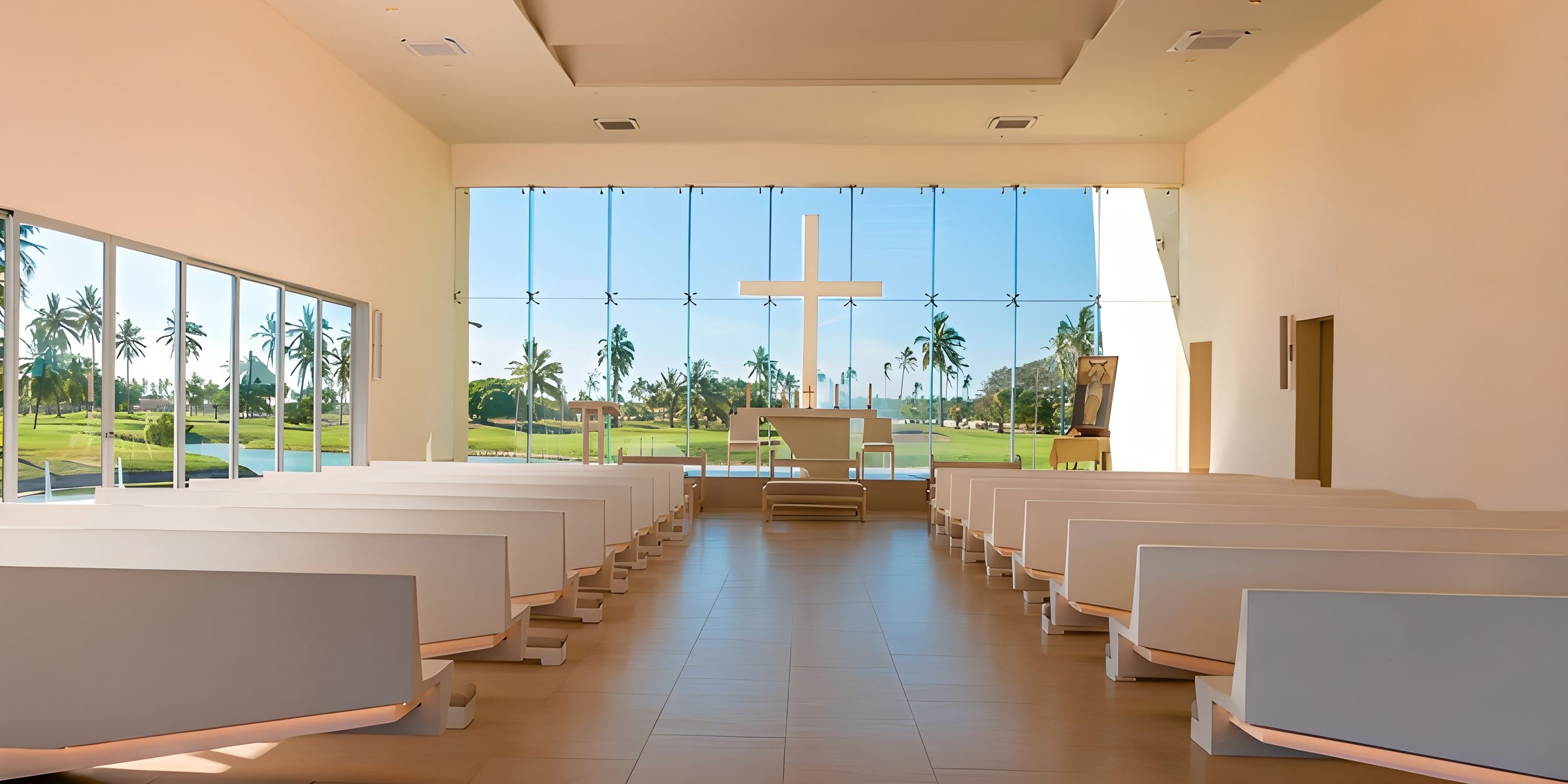 Modern chapel set for a destination wedding, with white pews, big windows, and cross facing palms.