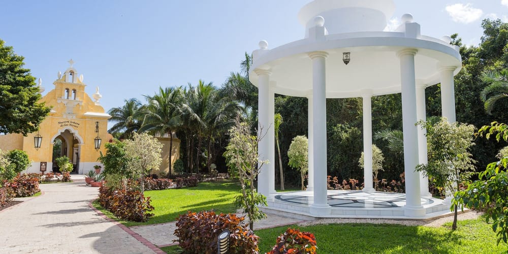 Charming yellow chapel and white gazebo in lush greenery, perfect for a destination wedding scene.