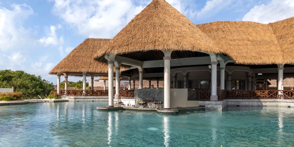 Thatched-roof poolside bar, perfect for a destination wedding with clear blue water and sky.