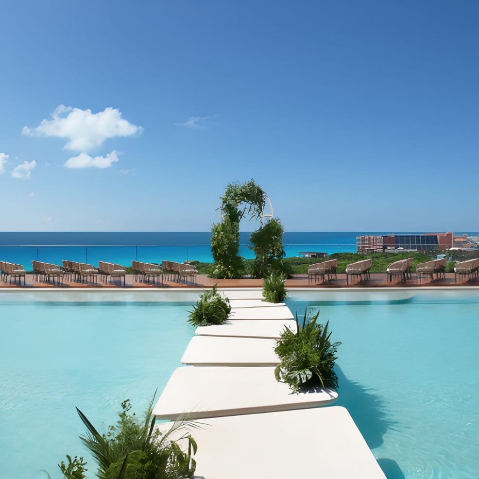 Destination wedding setup with chairs facing a floral arch over a pool overlooking the ocean.