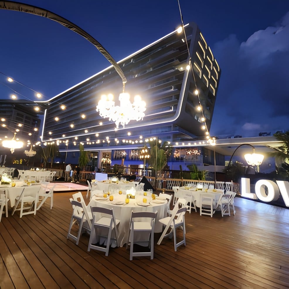 Destination wedding reception with dining tables on a wooden deck at dusk.