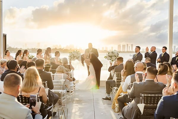 A bride and groom kiss at a sunset destination wedding at Mondrian Cancun as guests applaud.