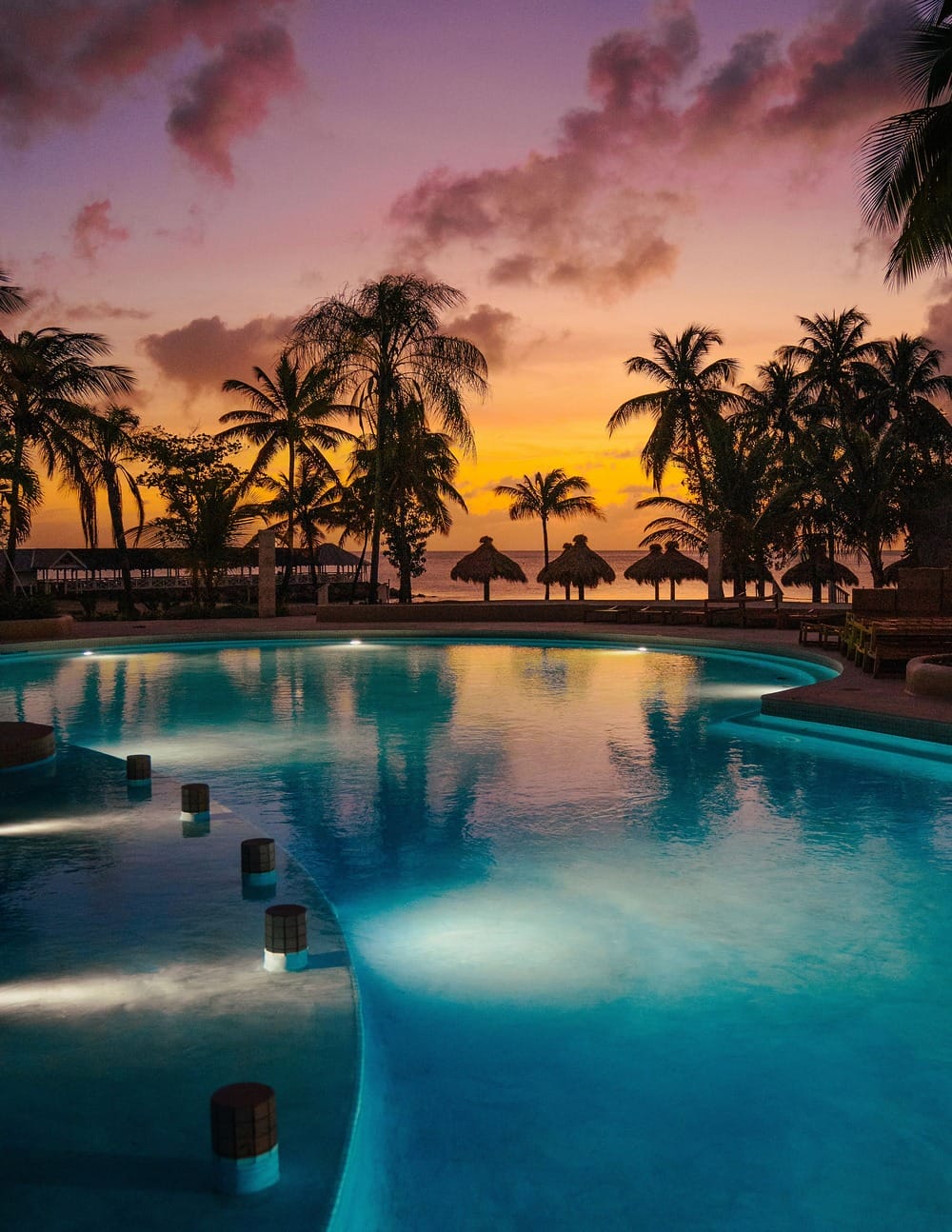 Illuminated pool with palm trees and a sunset sky, perfect for a dreamy destination wedding.