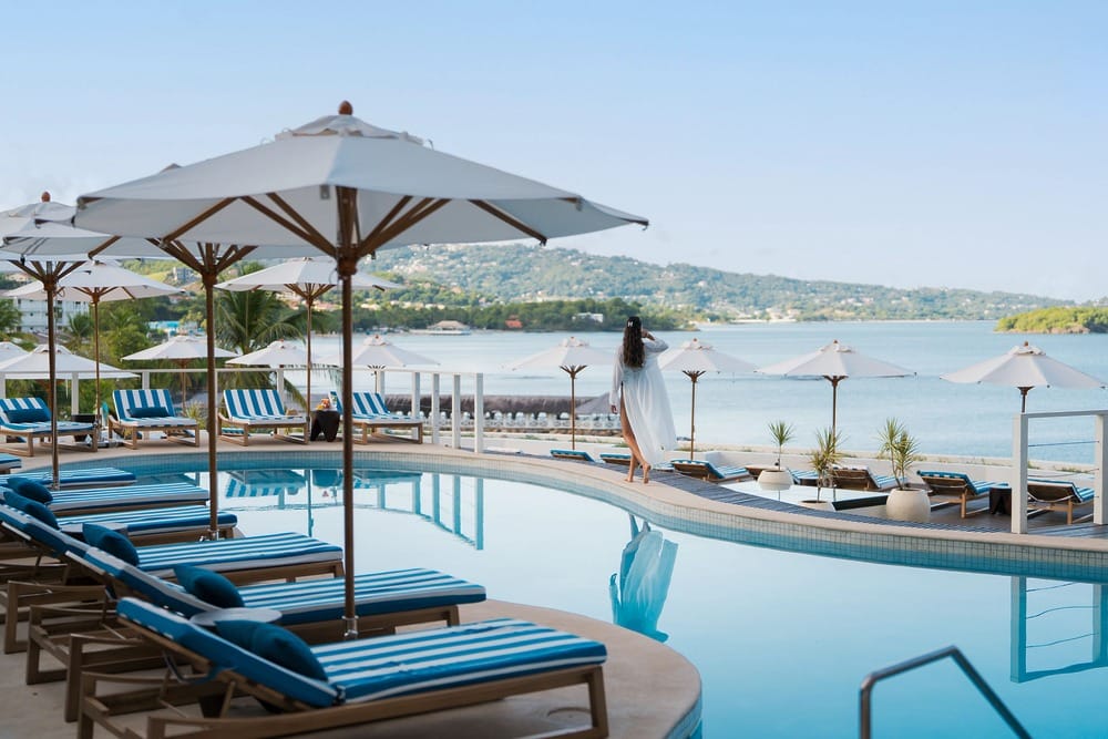 Poolside lounge chairs and umbrellas, perfect for a destination wedding by a calm bay with a guest.