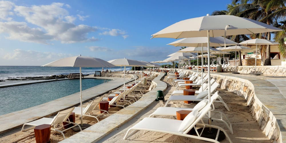 White lounge chairs and umbrellas line a beachfront pool, perfect for a destination wedding scene.