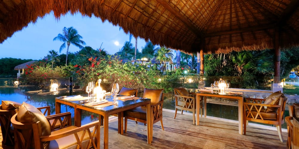 Open-air restaurant with wooden tables by water at dusk, perfect for a destination wedding.