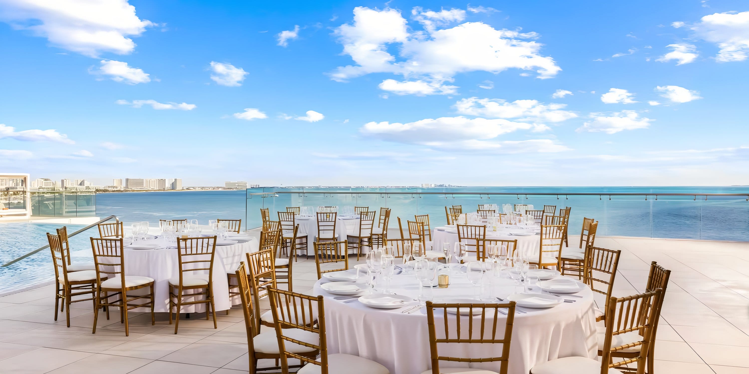 Elegant round tables with white linens and gold chairs set for a destination wedding terrace.