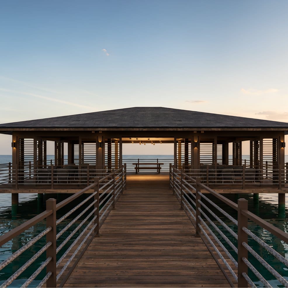 A wooden pier with a covered seating area, perfect for a destination wedding, over sunset-lit water.