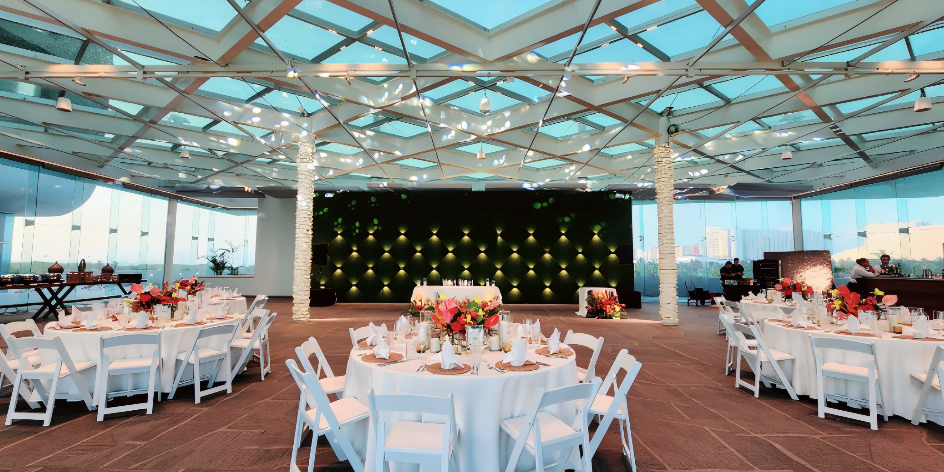 Wedding tables set in a glass-roofed event space with a lit geometric backdrop.