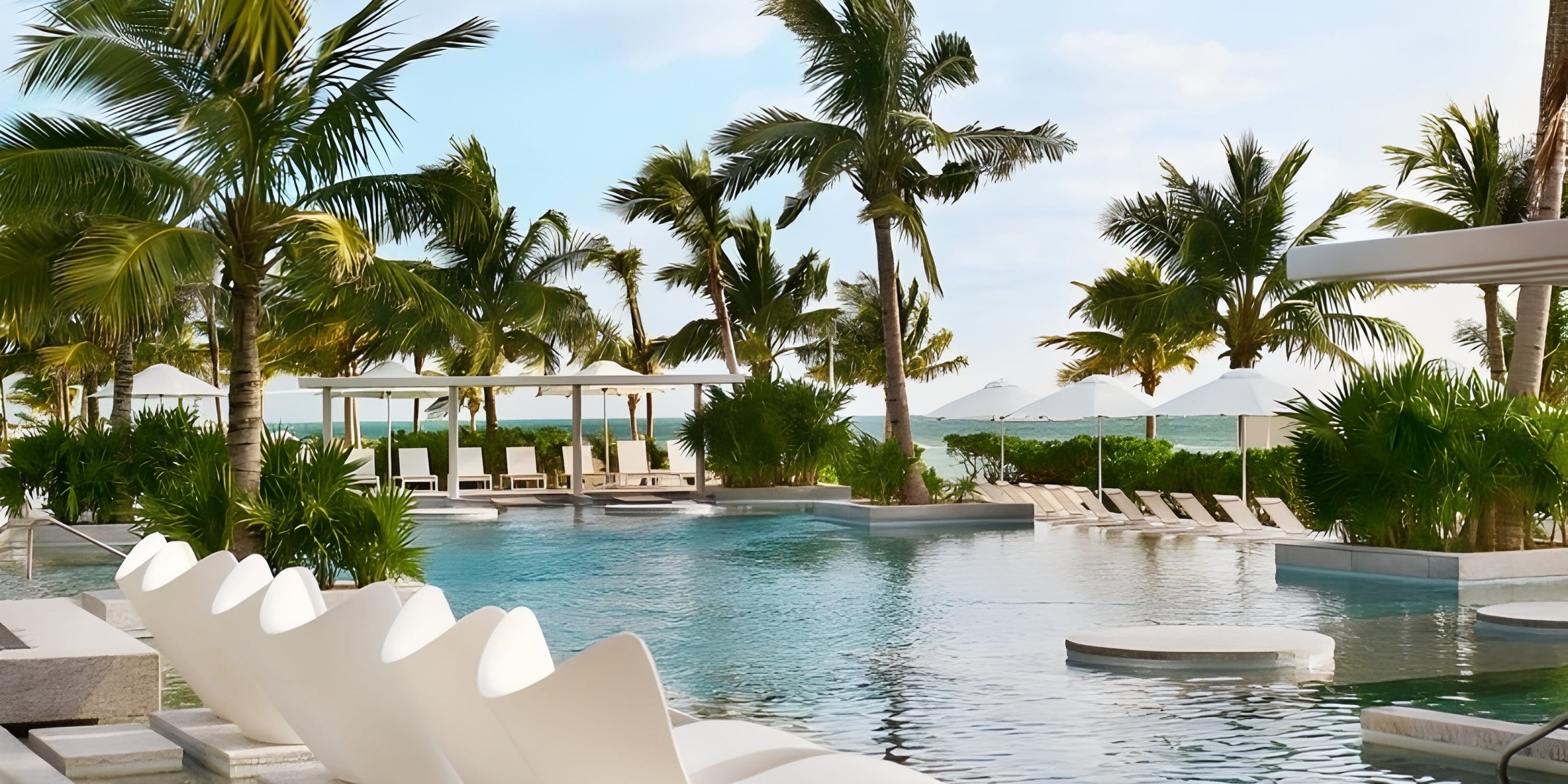 Swimming pool with lounge chairs and palms at SLS Playa Mujeres, a destination wedding venue.