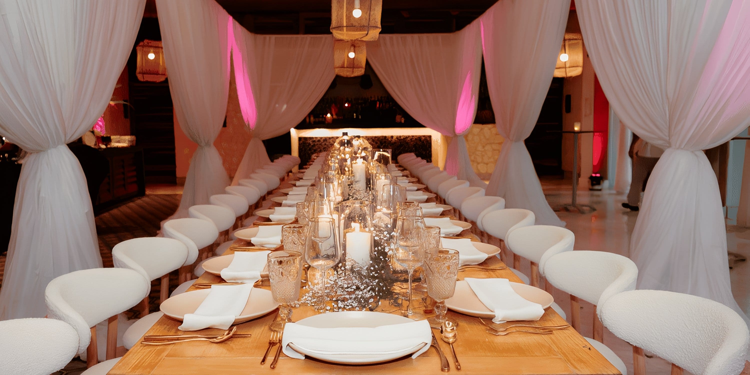 Long banquet table at a Dreams Playa Mujeres destination wedding with white drapes and candles.