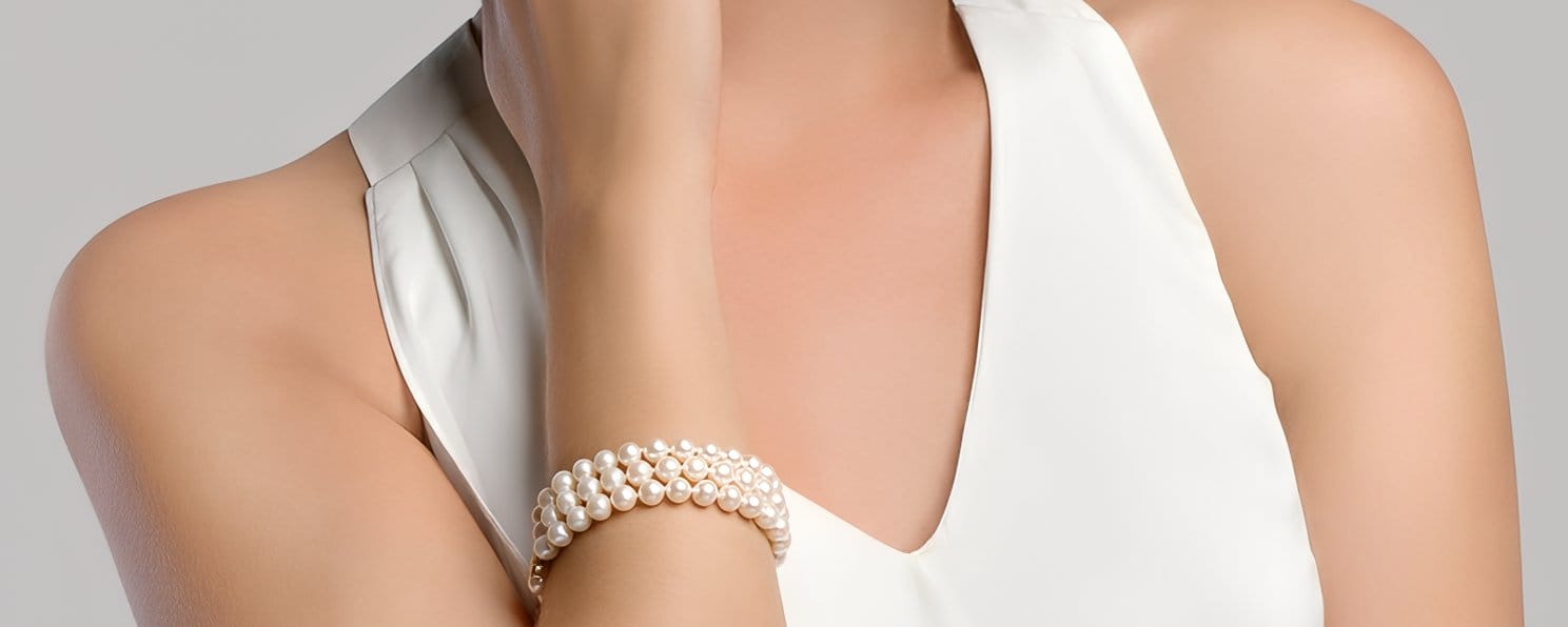 Woman in a white dress wearing a triple-strand pearl bracelet for a wedding.