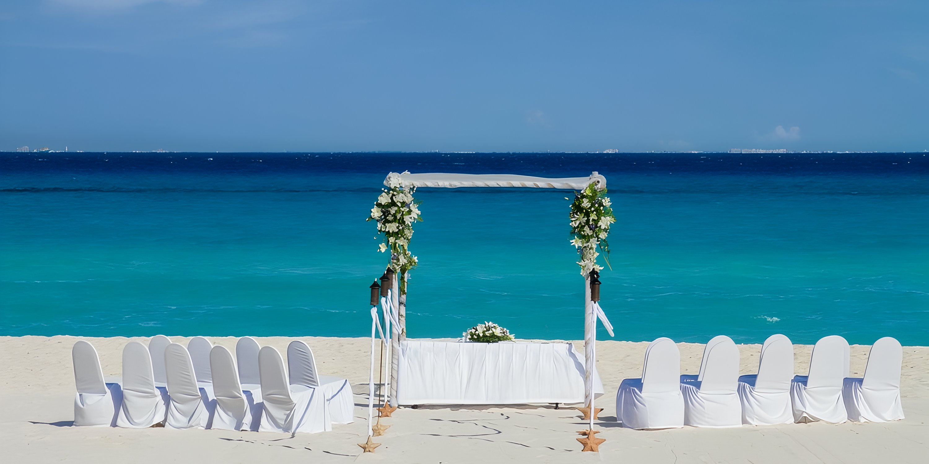 Wedding floral arch and white chairs on the sand at Viva Maya by Wyndham-All Inclusive Resort.