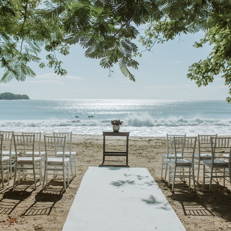 White chairs face a floral centerpiece at this beach destination wedding altar.