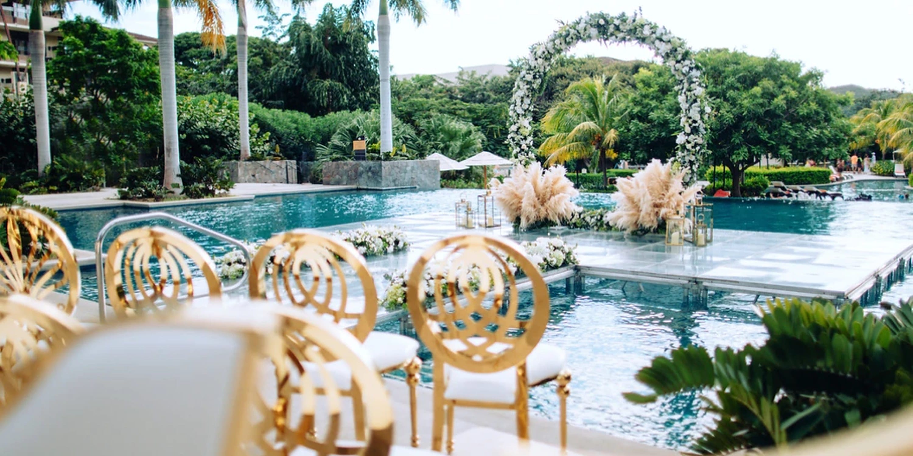 Destination wedding ceremony set up on a platform over a swimming pool with a floral arch.