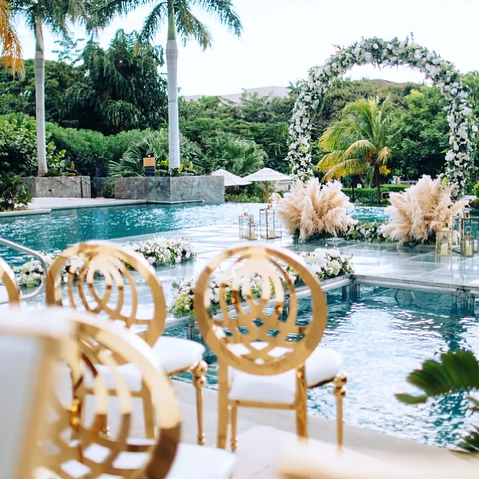 Gold wedding chairs face a floral arch over a pool at a destination wedding.