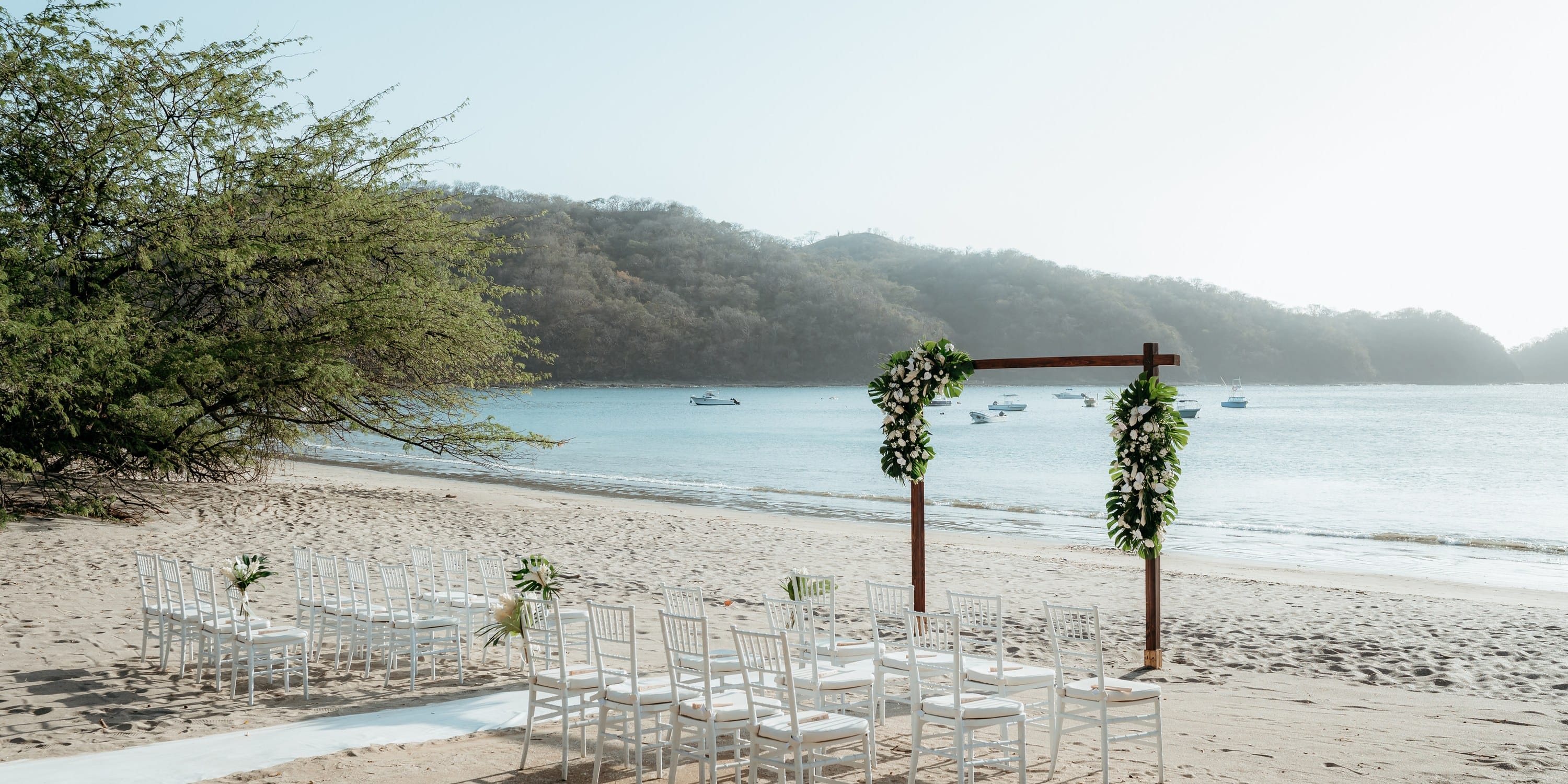 White chairs set up for a destination wedding ceremony on a tropical beach.