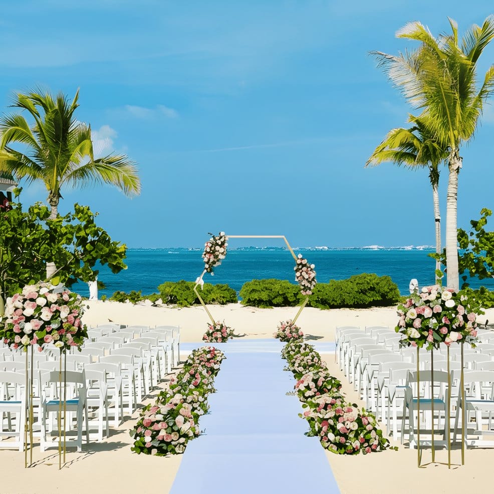 A destination wedding setup on a beach featuring a hexagonal arch and floral arrangements.