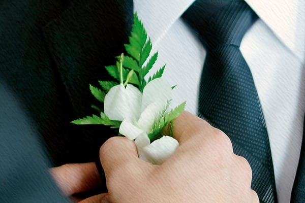 Hand adjusting a white floral wedding boutonniere on a dark suit lapel at SLS Playa Mujeres.