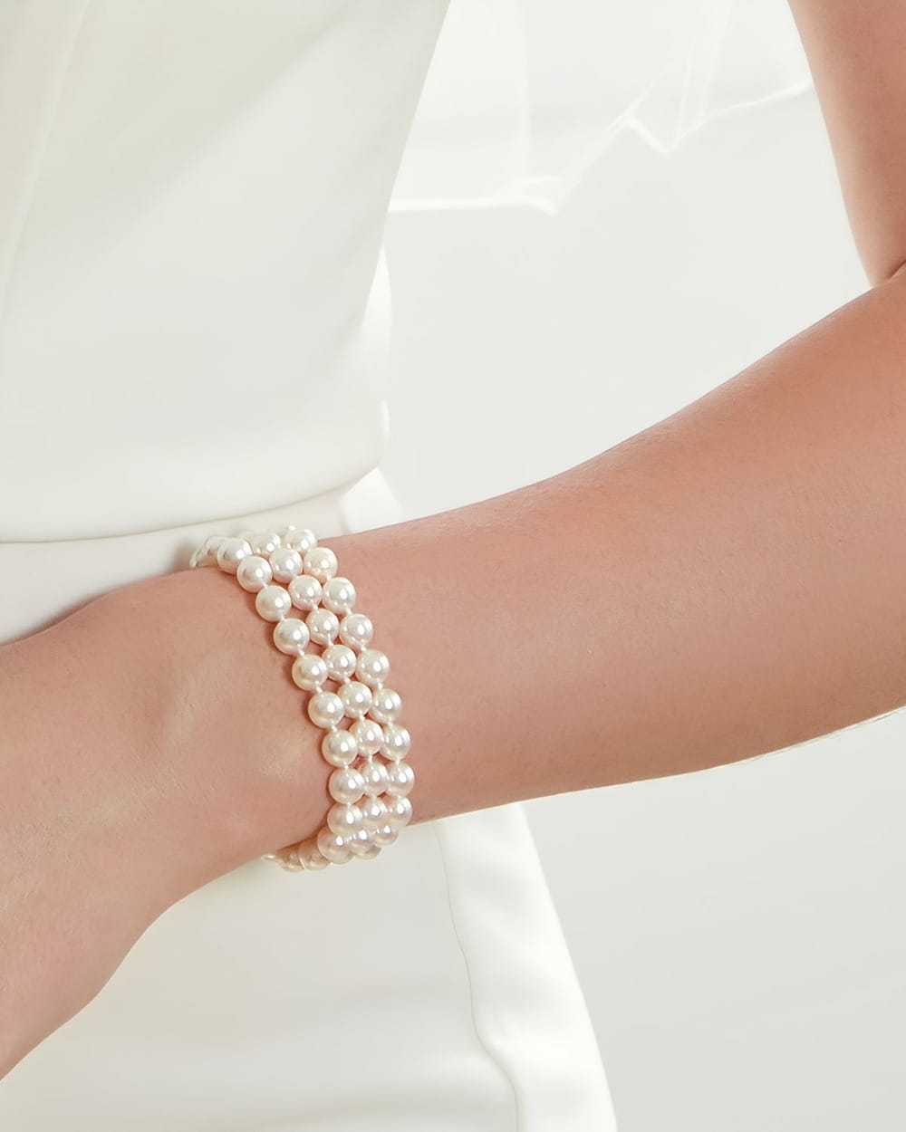 Three-strand pearl bracelet worn by a person in a white wedding dress.